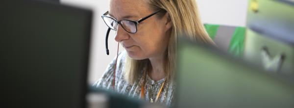 An Eastlight staff member answering a phone call in Eastlight's Braintree hub offices. The female member of staff is wearing a headset and glasses, and is looking down slightly, towards a computer screen. 
