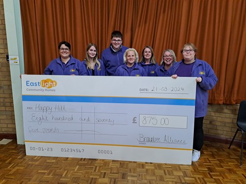 Members from Happy Hill in Braintree are stood behind a huge cardboard cheque that says £875 has been awarded to them.