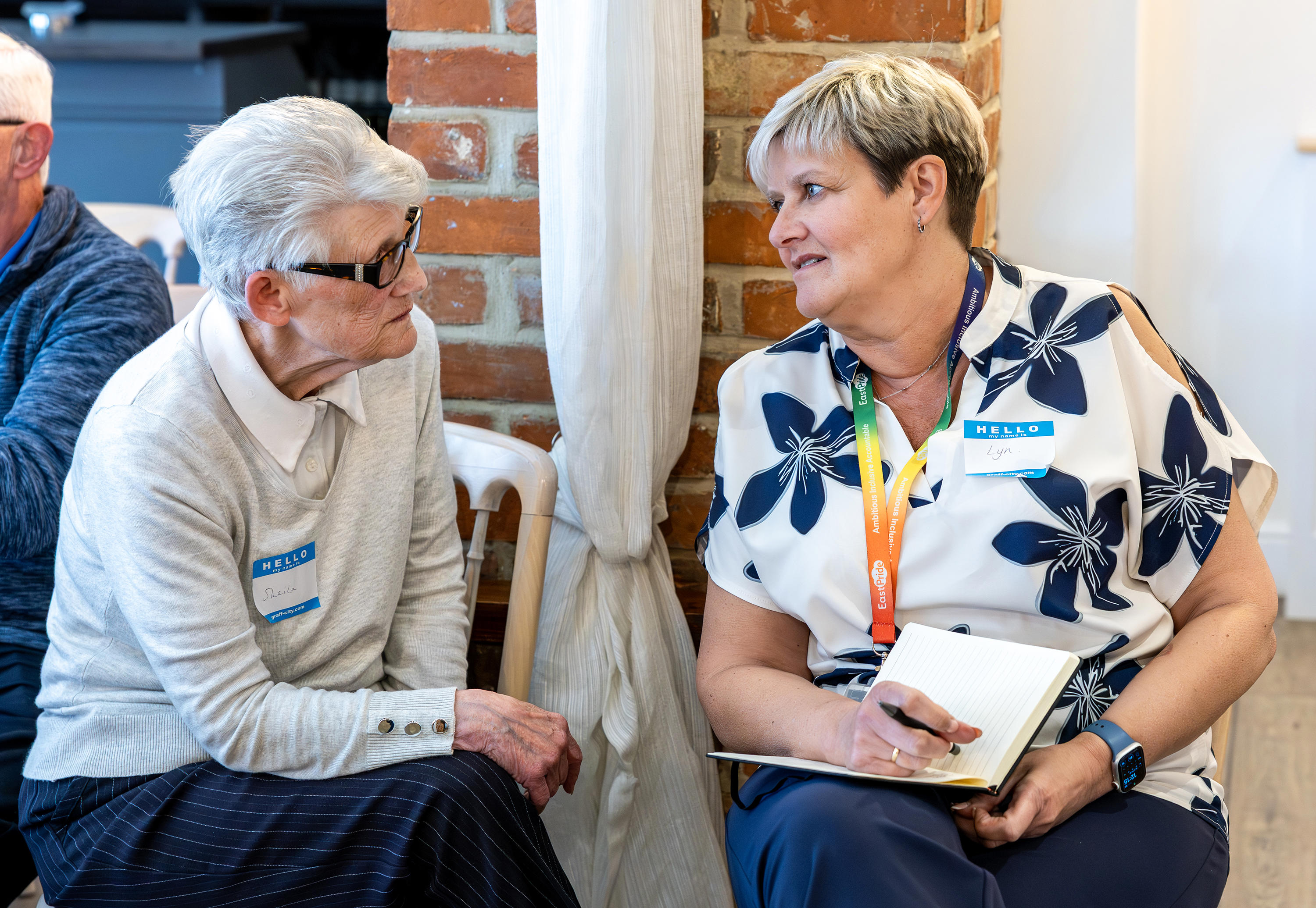 Two women are sat side by side talking to each other.