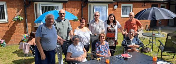 A group of residents are sat around a table at a BBQ.