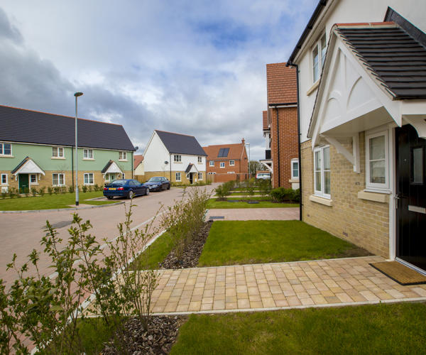 Two rows of houses are facing each other with a road in the middle. Cars are parked along the road.