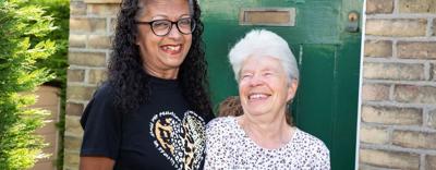 Eastlight residents Abaida and Joy, standing together on a front door step, smiling at the camera. The front door behind them is a dark green colour. To the left of the door is the house number 30. 