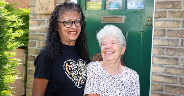 Eastlight residents Abaida and Joy, standing together on a front door step, smiling at the camera. The front door behind them is a dark green colour. To the left of the door is the house number 30. 