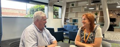 Former Eastlight Board member, Dale Butcher, sat with past Dale Butcher Work Experience Programme participant, Wendy Harris, in the downstairs cafe area of Eastlight House, Braintree. They are sitting at a table facing each other, smiling and chatting. There are two mugs of tea on the table, each with the Eastlight logo on them. The Eastlight offices are visible in the background.