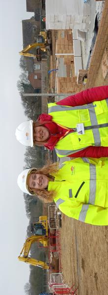 Eastlight development manager, Debbie Mitchell, and work experience attendee Wendy Richards, are stood next to each other on a building site.  They are both wearing hi-vis jackets and white hard hats.