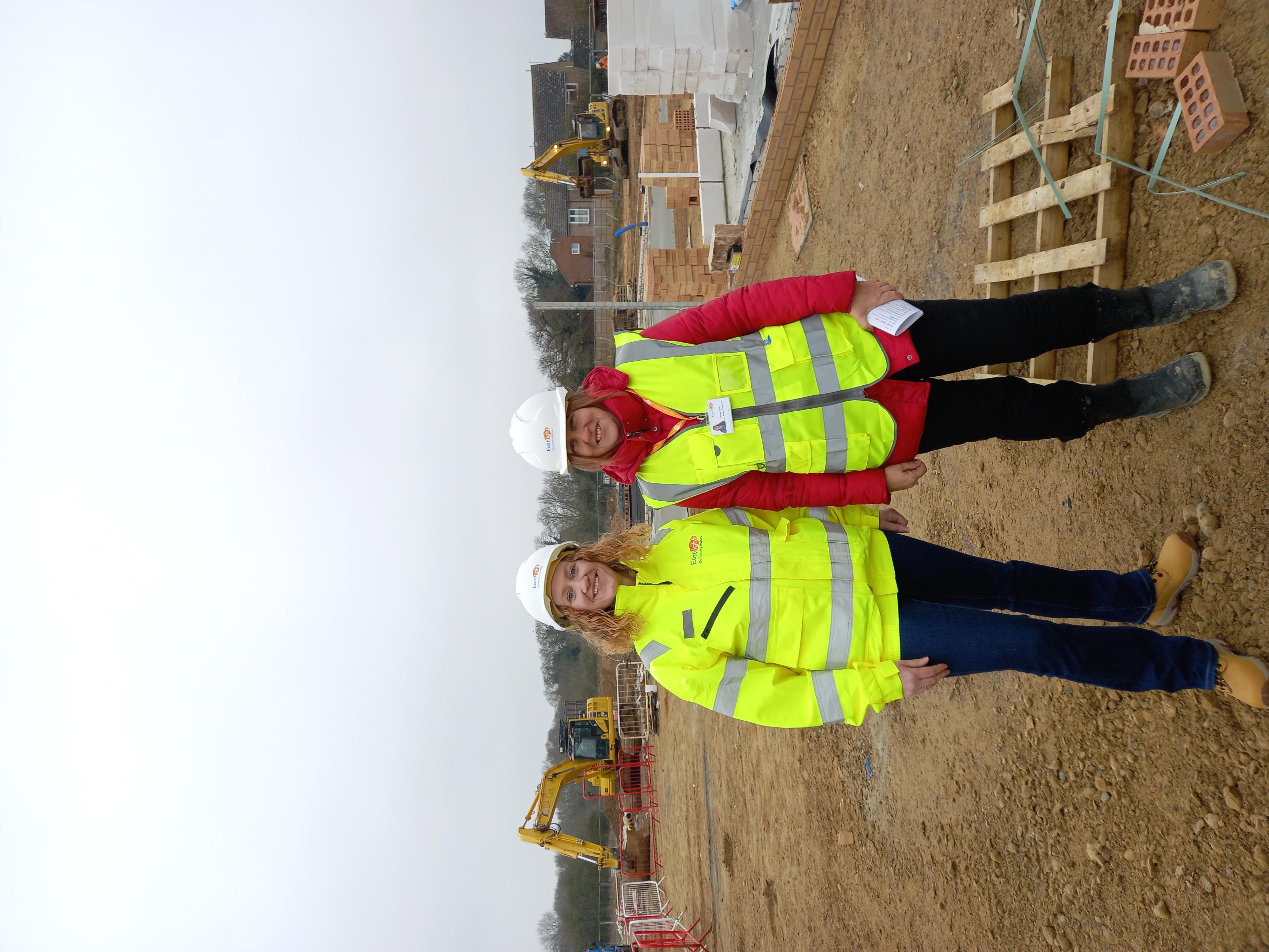 Eastlight development manager, Debbie Mitchell, and work experience attendee Wendy Richards, are stood next to each other on a building site.  They are both wearing hi-vis jackets and white hard hats.