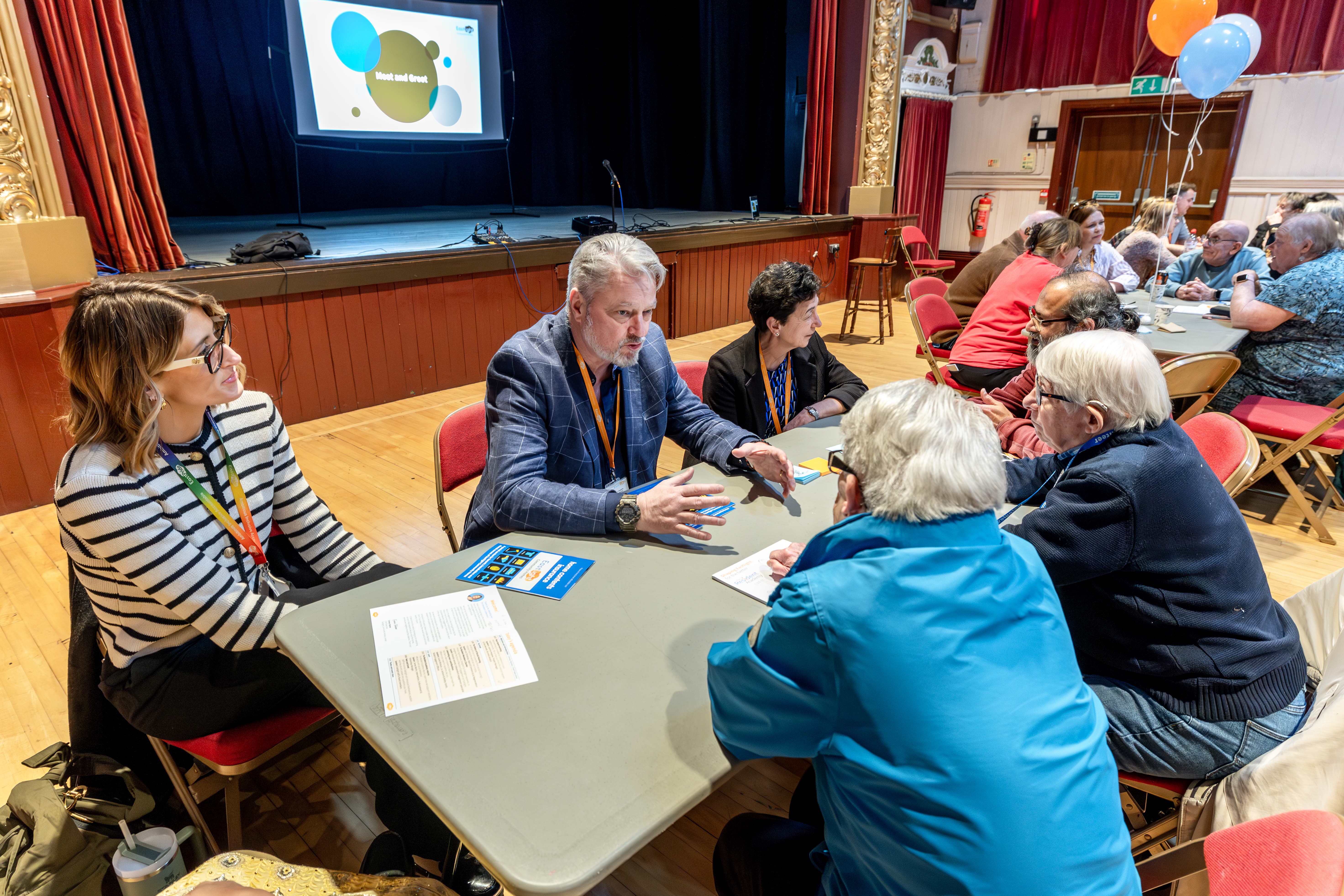 A group of residents and staff are sat around a table talking.